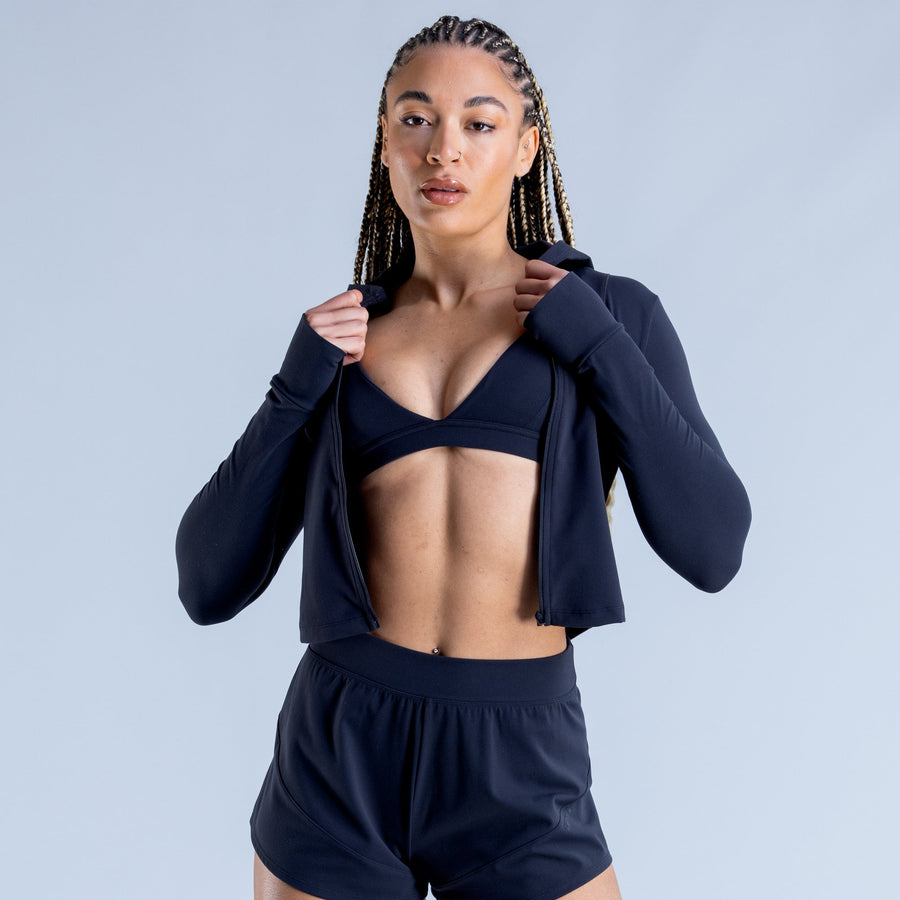 Navy hooded zip-up cropped jacket over black sports bra and athletic shorts set