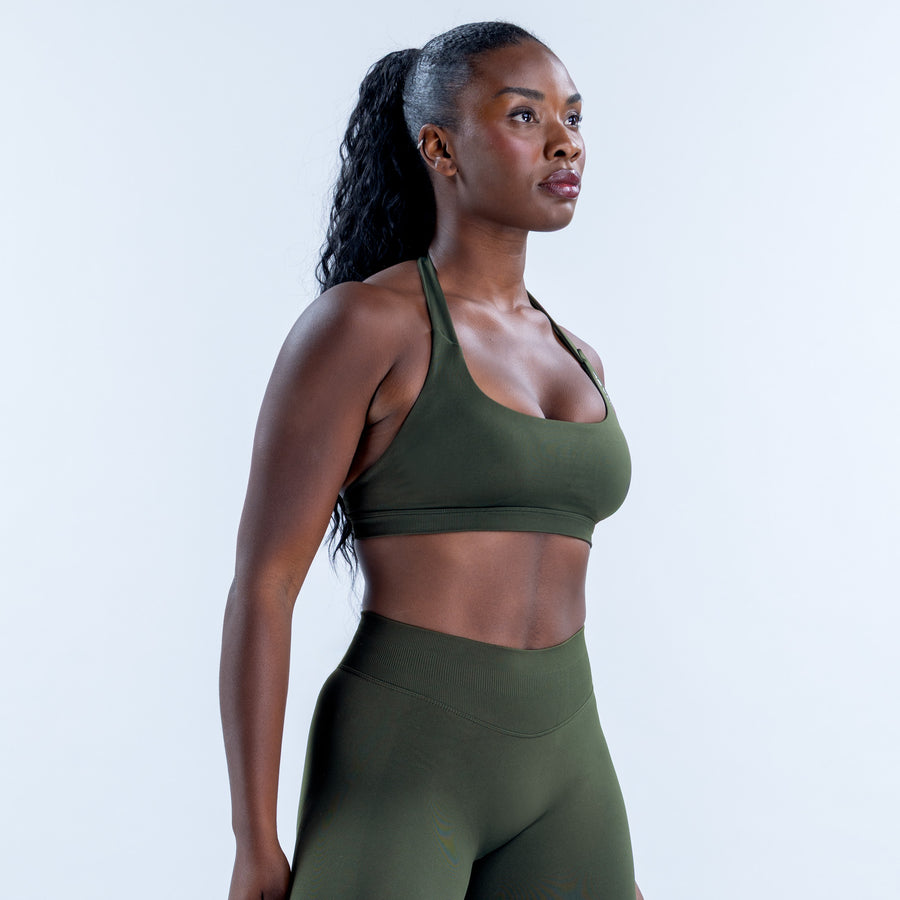 Dark green sports bra with a scoop neckline and broad shoulder straps, shown at an angle